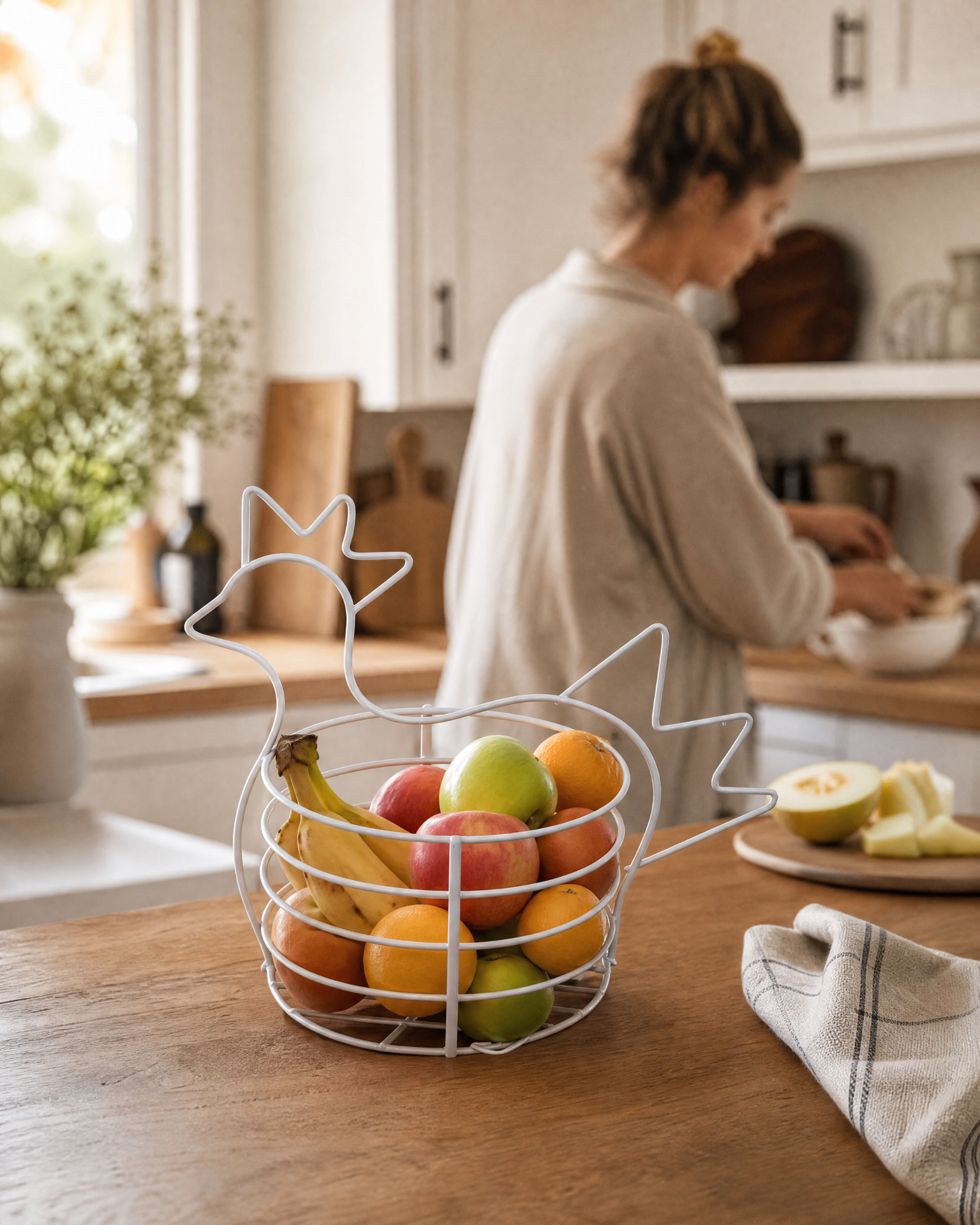 Mujer cocinando junto a la Gallina Multiusos GINLU llena de frutas frescas en una cocina luminosa y ordenada